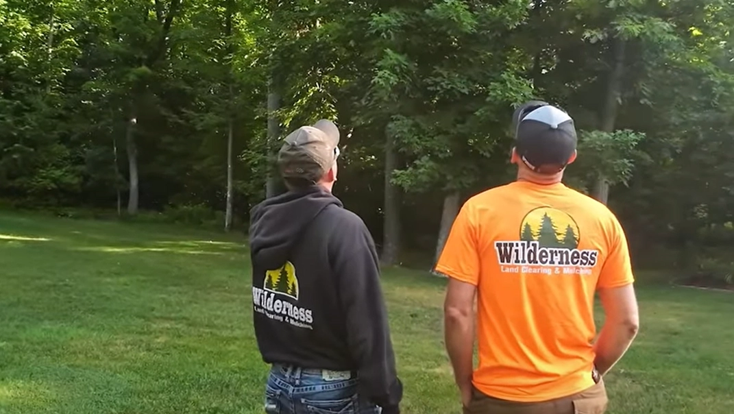 Two Wilderness Land Clearing workers looking at a tree.