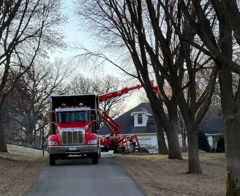 A dump truck is parked in front of a house for tree trimming.
