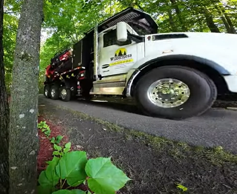 A Wilderness Land Clearing truck parked in a wooded driveway.